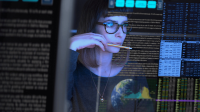 An adult female OSU student sits in front of a screen that displays cybersecurity information.