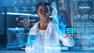 In a medical room setting an Ohio State health professional in a white lab coat stands behind a screen revealing AI elements, including a rendering of the human body.  