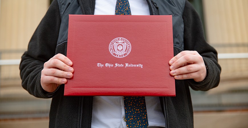 An Ohio State graduate proudly displays his diploma on the steps of Page Hall.