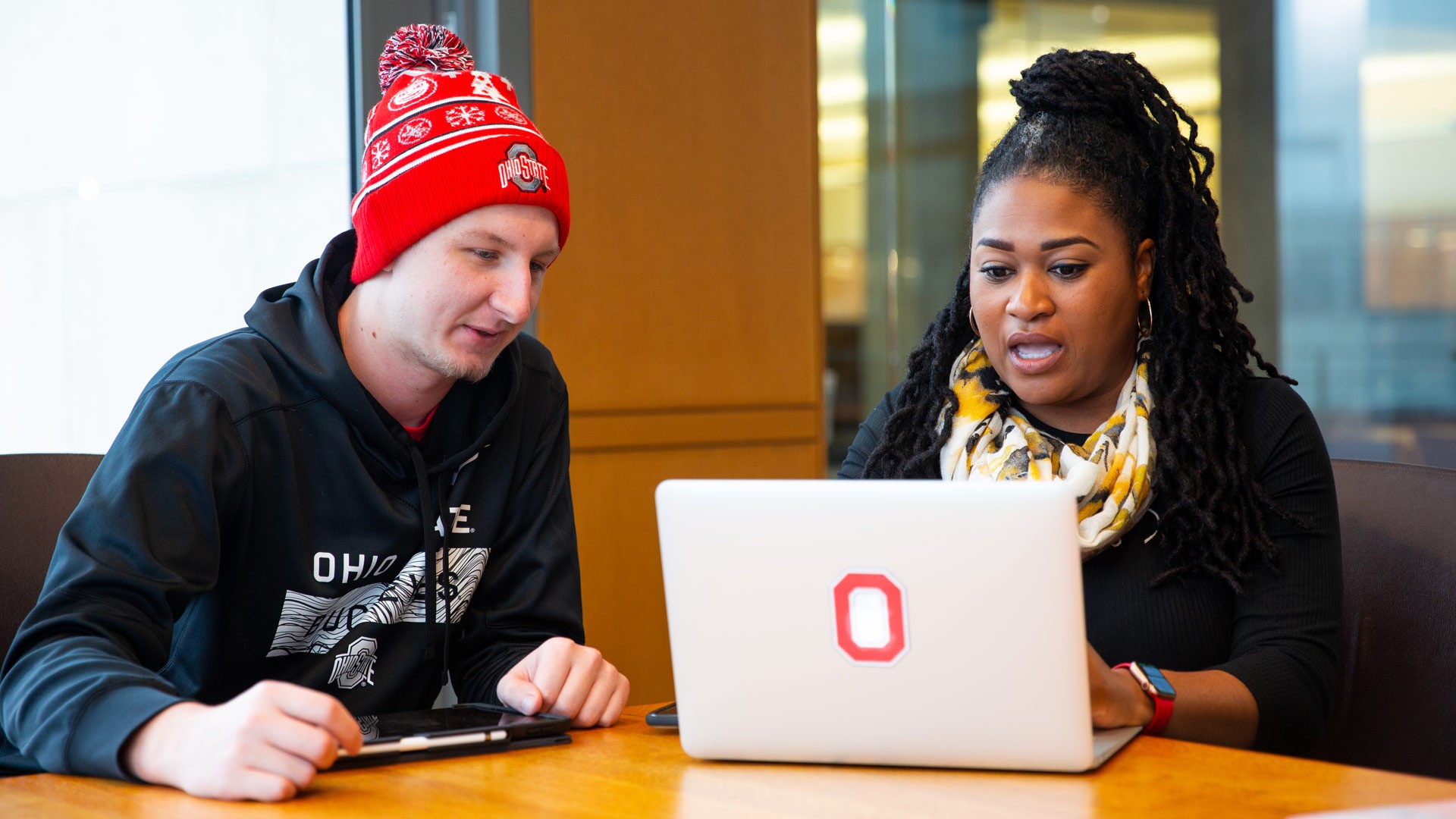 Two seated people looking at a laptop computer together researching the cost of online degrees.