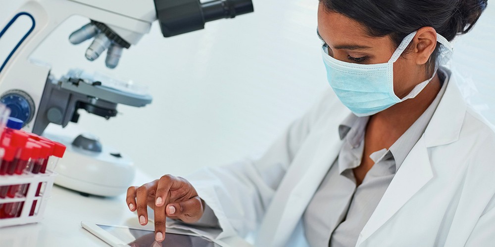 Woman wearing a lab coat and mask using a tablet in a research lab