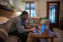 Student completes work for an online certificate program on a laptop in his living room.  