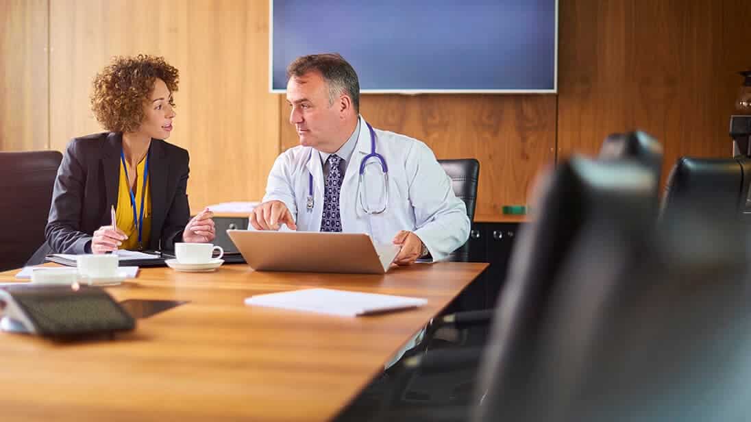 Doctor collaborates with woman at a conference table.