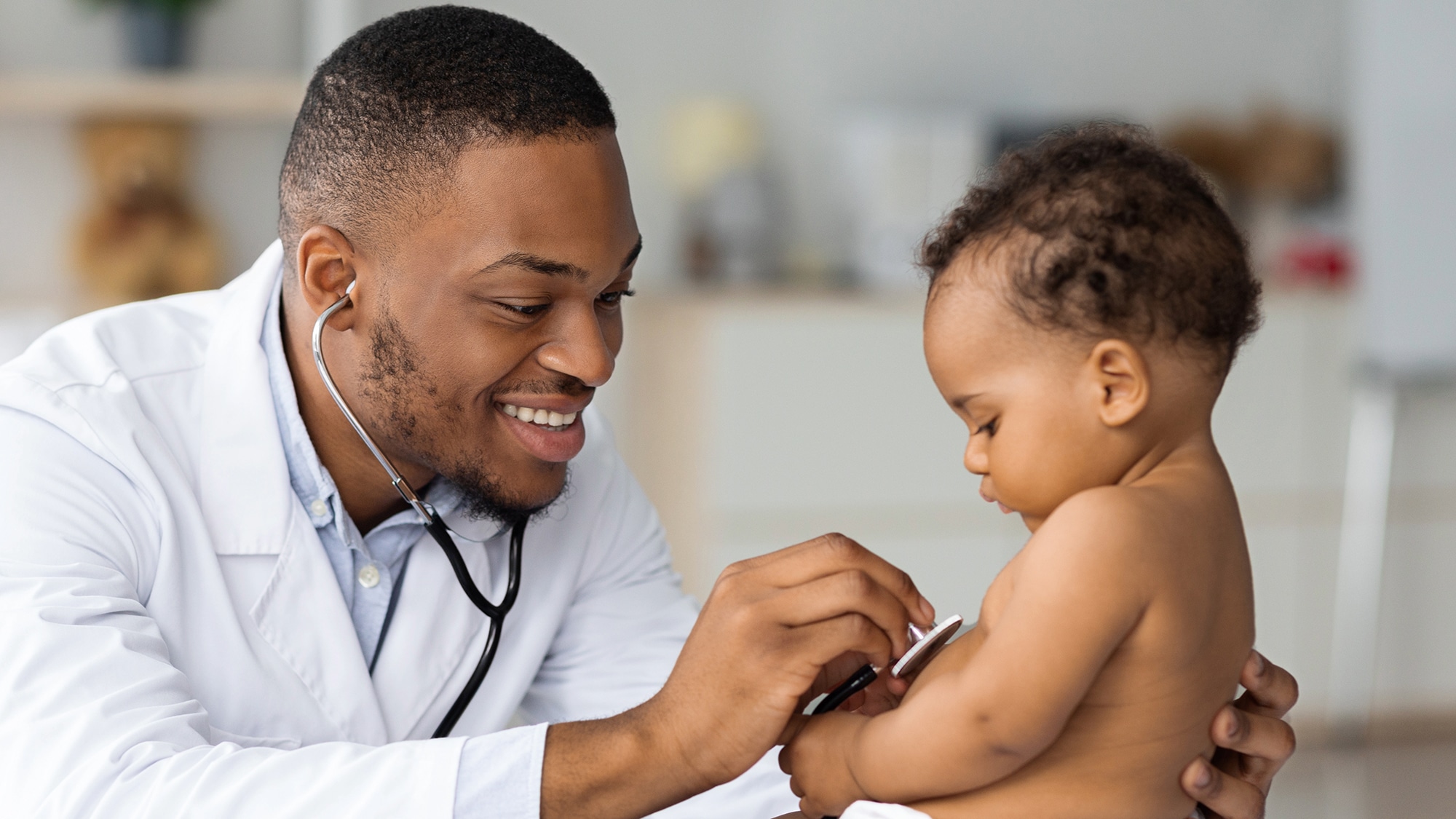 Male pediatric nurse practitioner in white coat cares for toddler patient
