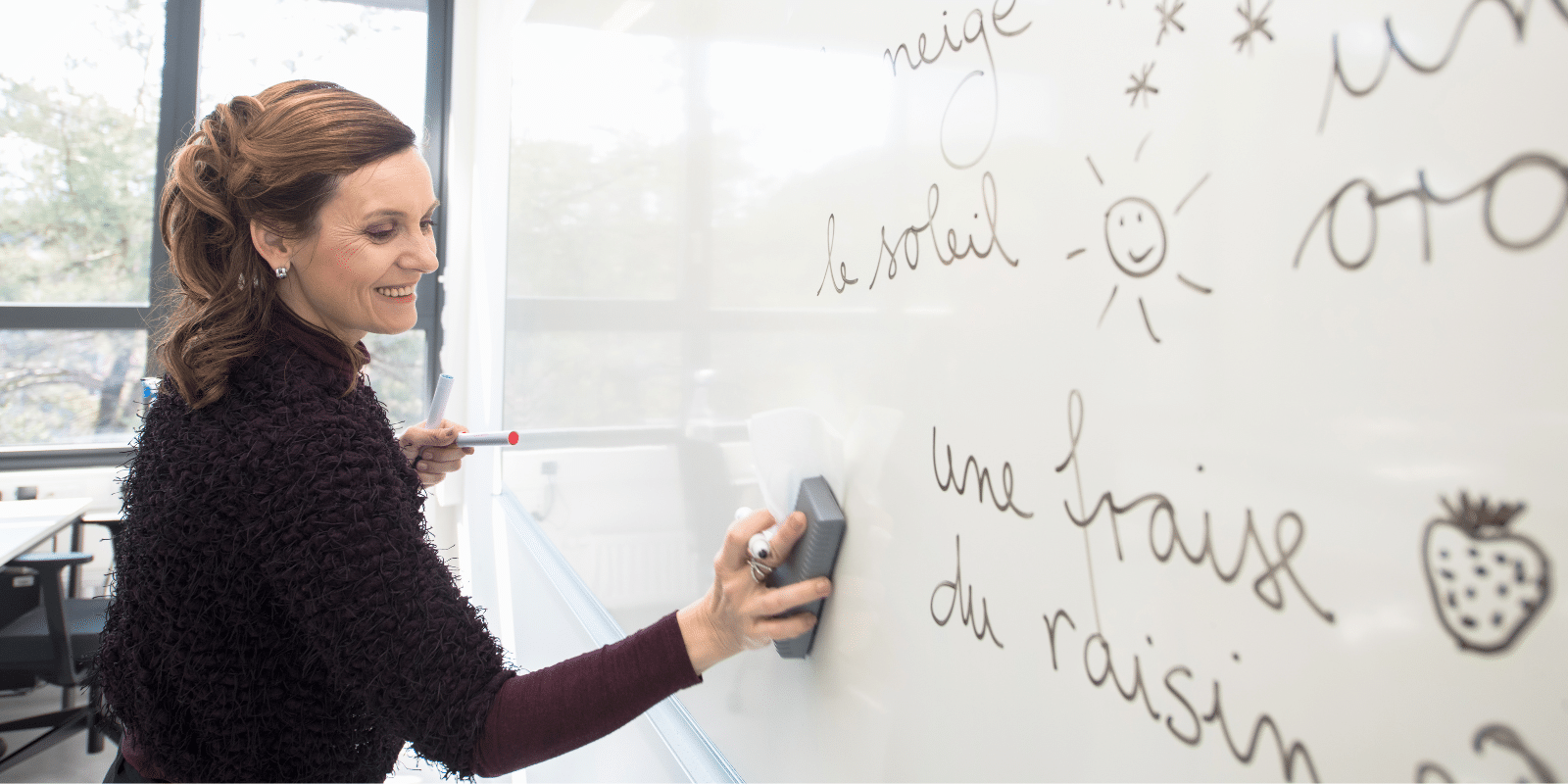 A teacher erases a white board with French vocabulary words on it