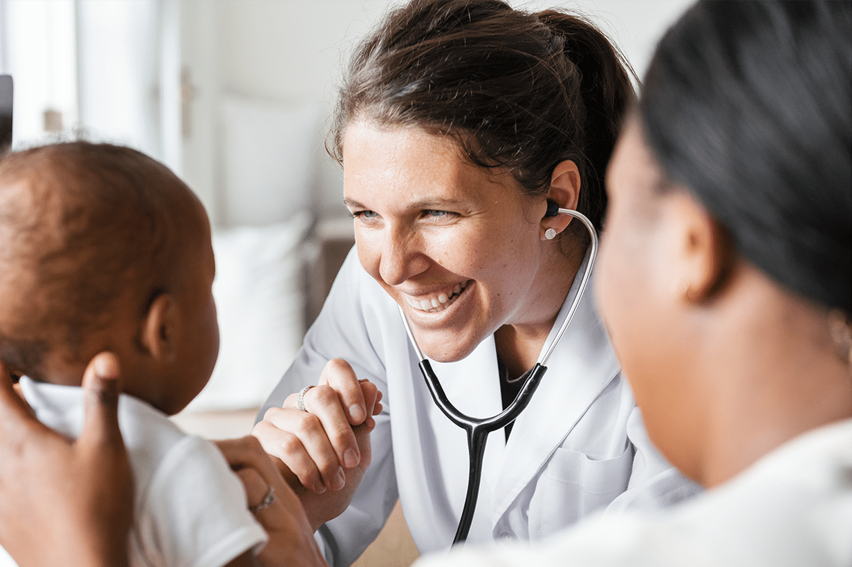 Nurse practitioner happily cares for infant patient whose mother is standing by.