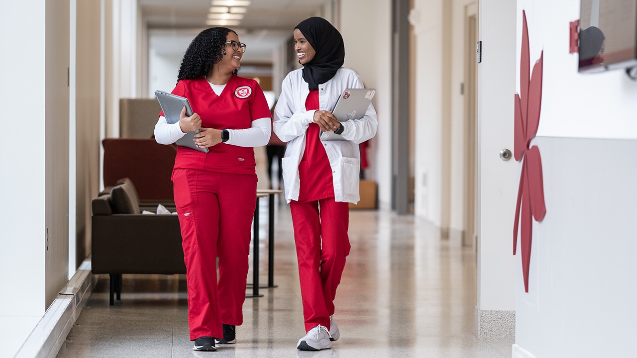 Two nurses in Ohio State scrubs walk down a hallway chatting.