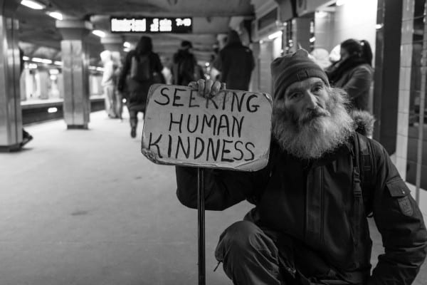Unhoused man holding a sign seeking assistance.