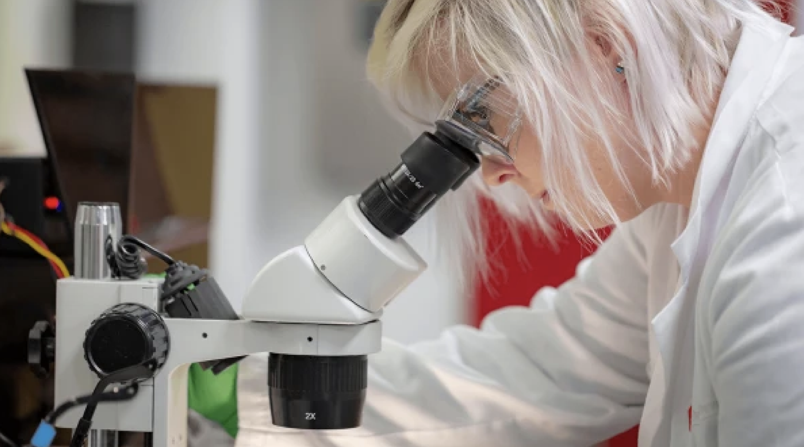 student in white lab coat looking through a microscope