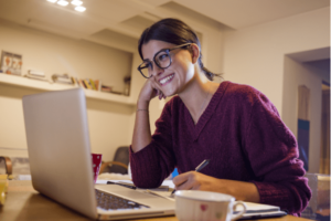 An online student smiles at her laptop as she practices being a sustainable online learner.