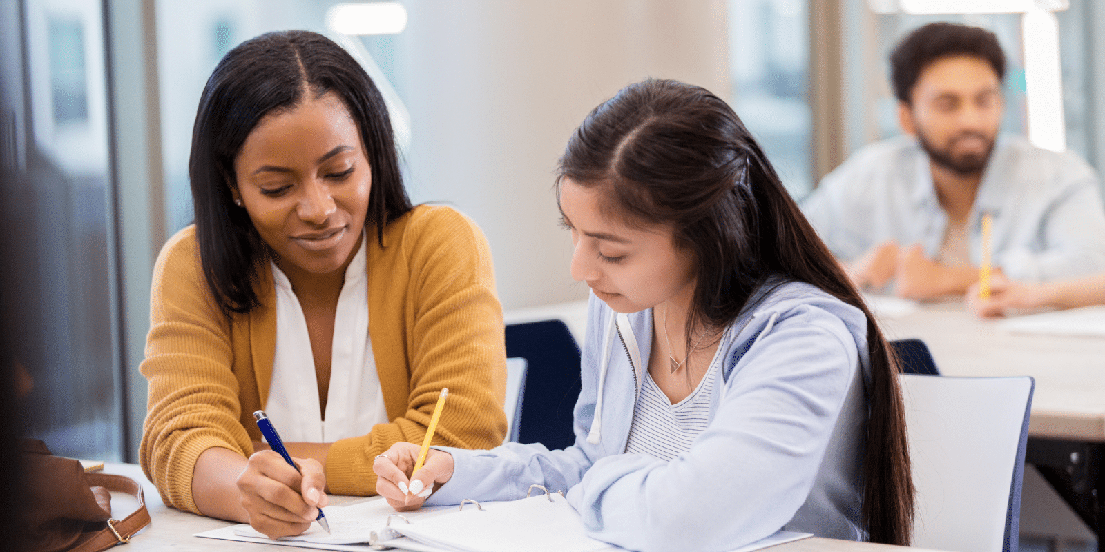 A teacher sits with a high school student at a desk