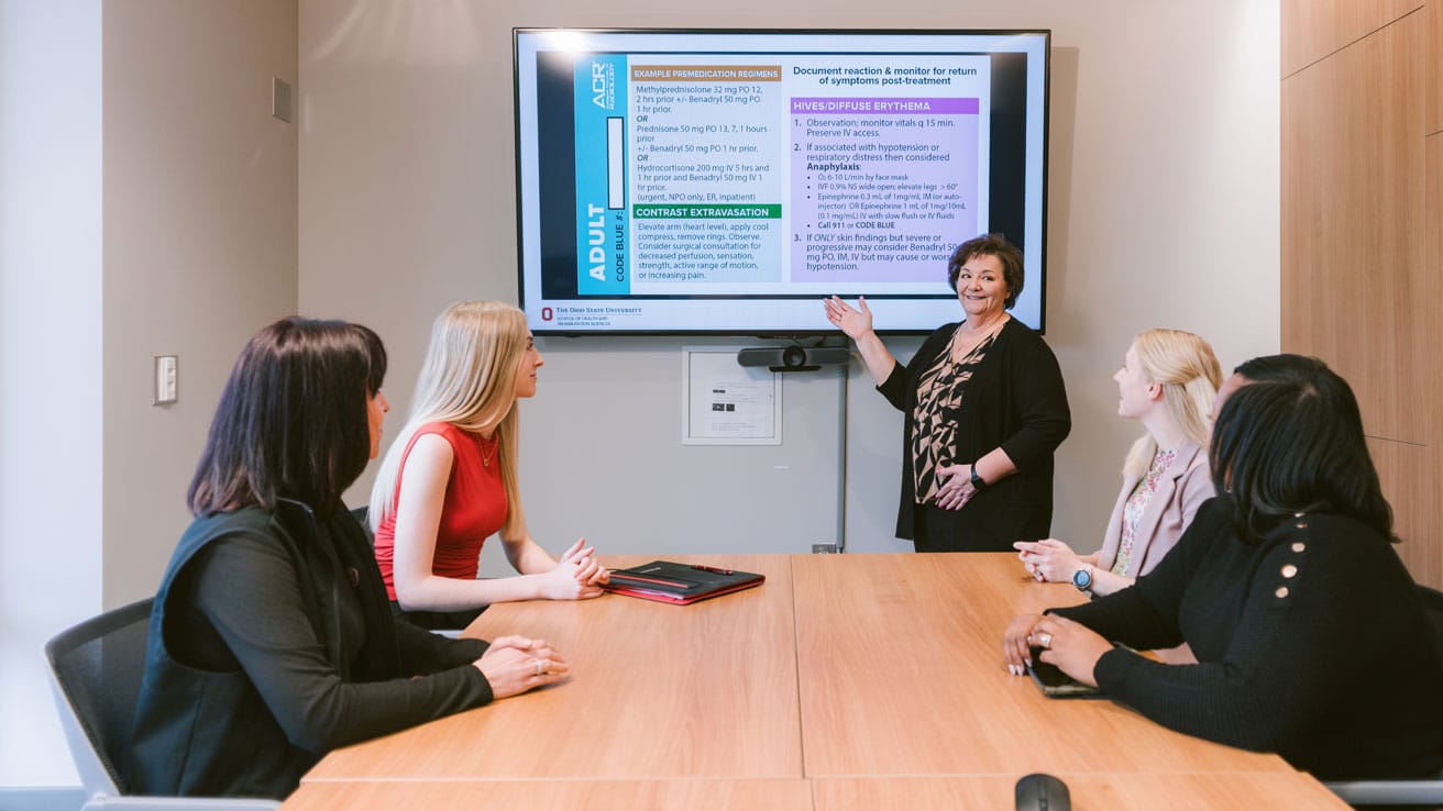 Tonette leading a presentation during a meeting standing in front of a screen.