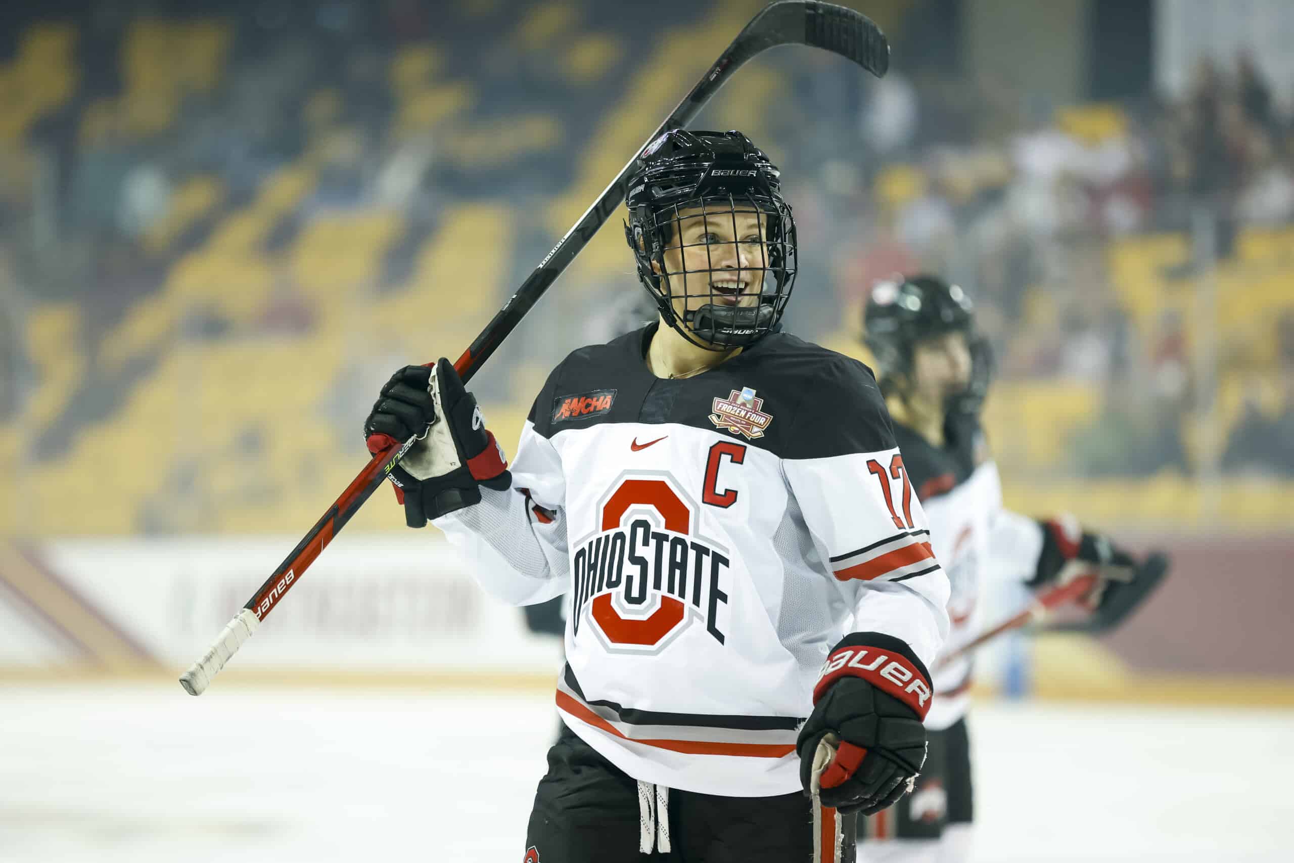 Emma Maltais, a white, blonde-haired female, wears team hockey uniform on Ohio State’s ice hockey rink, holding a hockey stick.