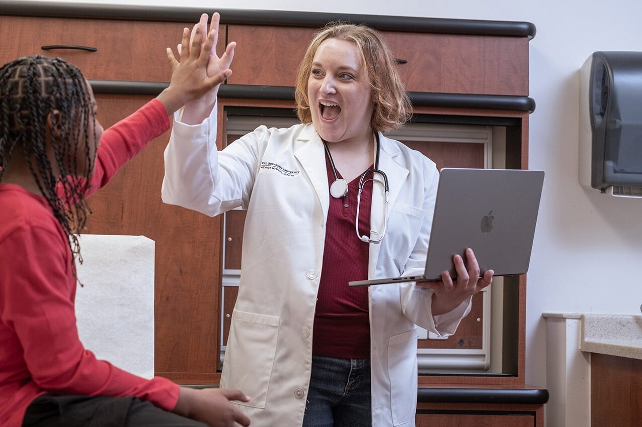 DNP-prepared nurse high-fives teen patient during a check-up.