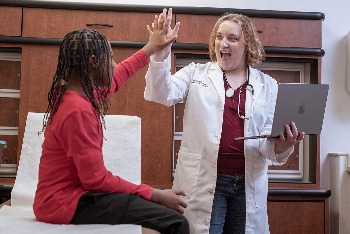 DNP-prepared nurse high-fives teen patient during a check-up.
