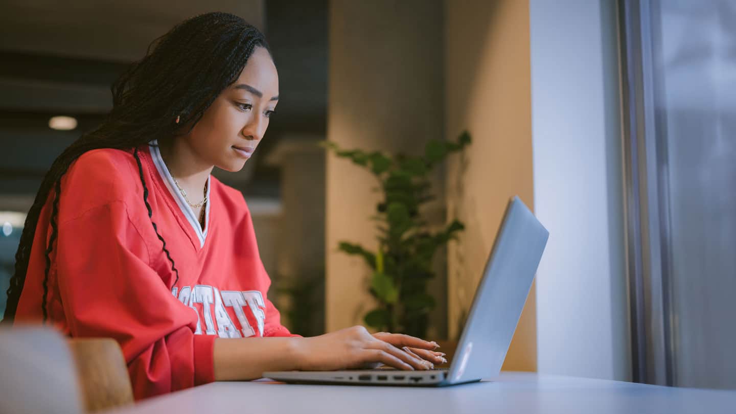 Female online student using a laptop at the library.
