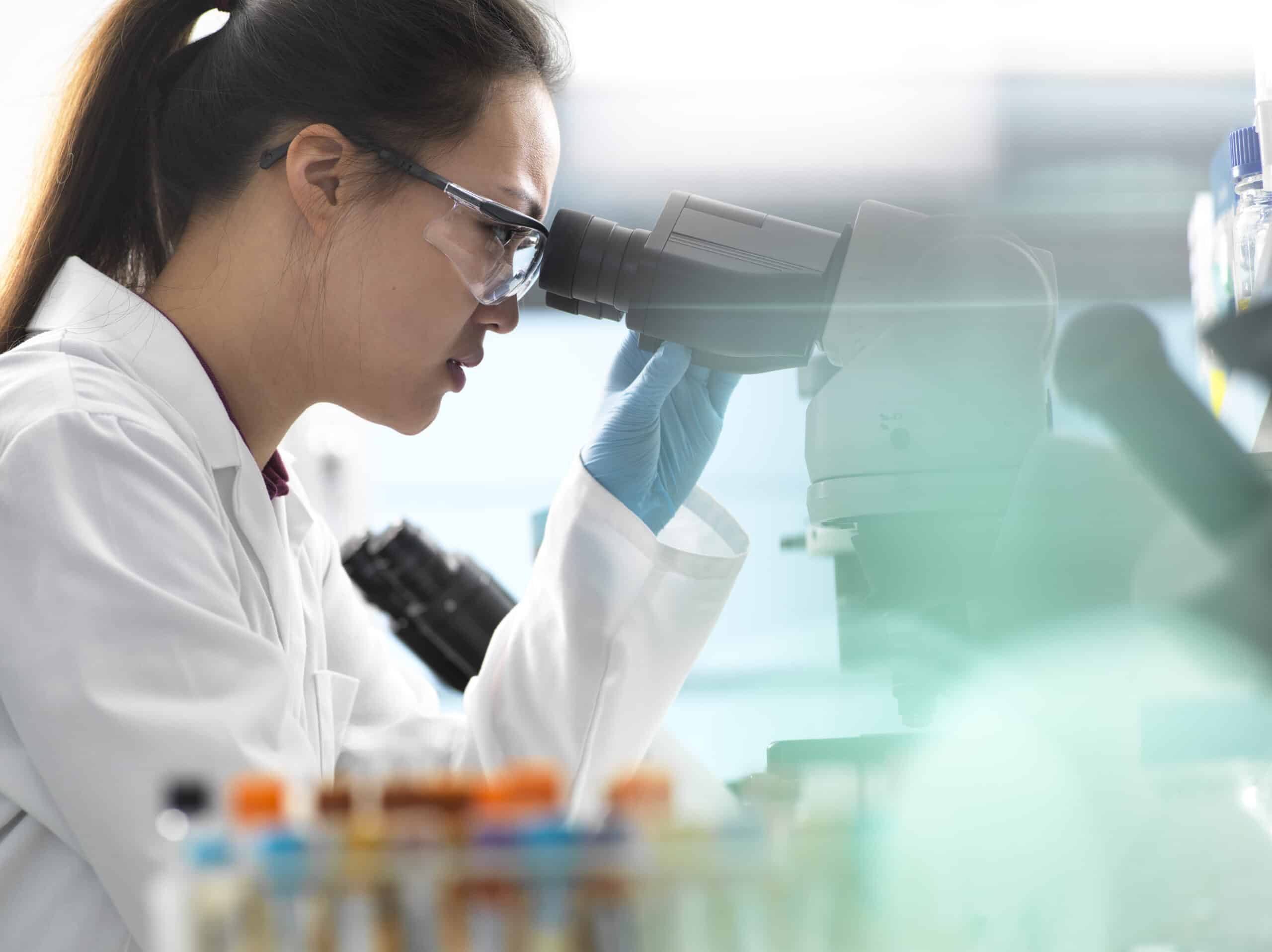 cientist viewing human sample on glass slide with microscope in laboratory