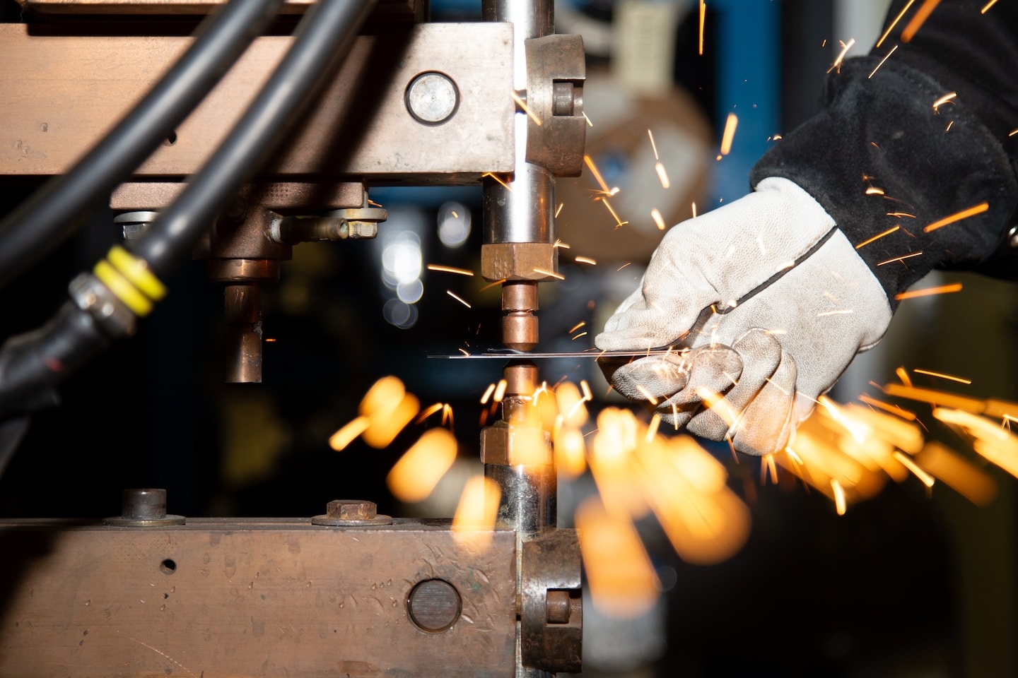 A welding engineer performs a spot weld on a piece of metal as sparks fly in the foreground.