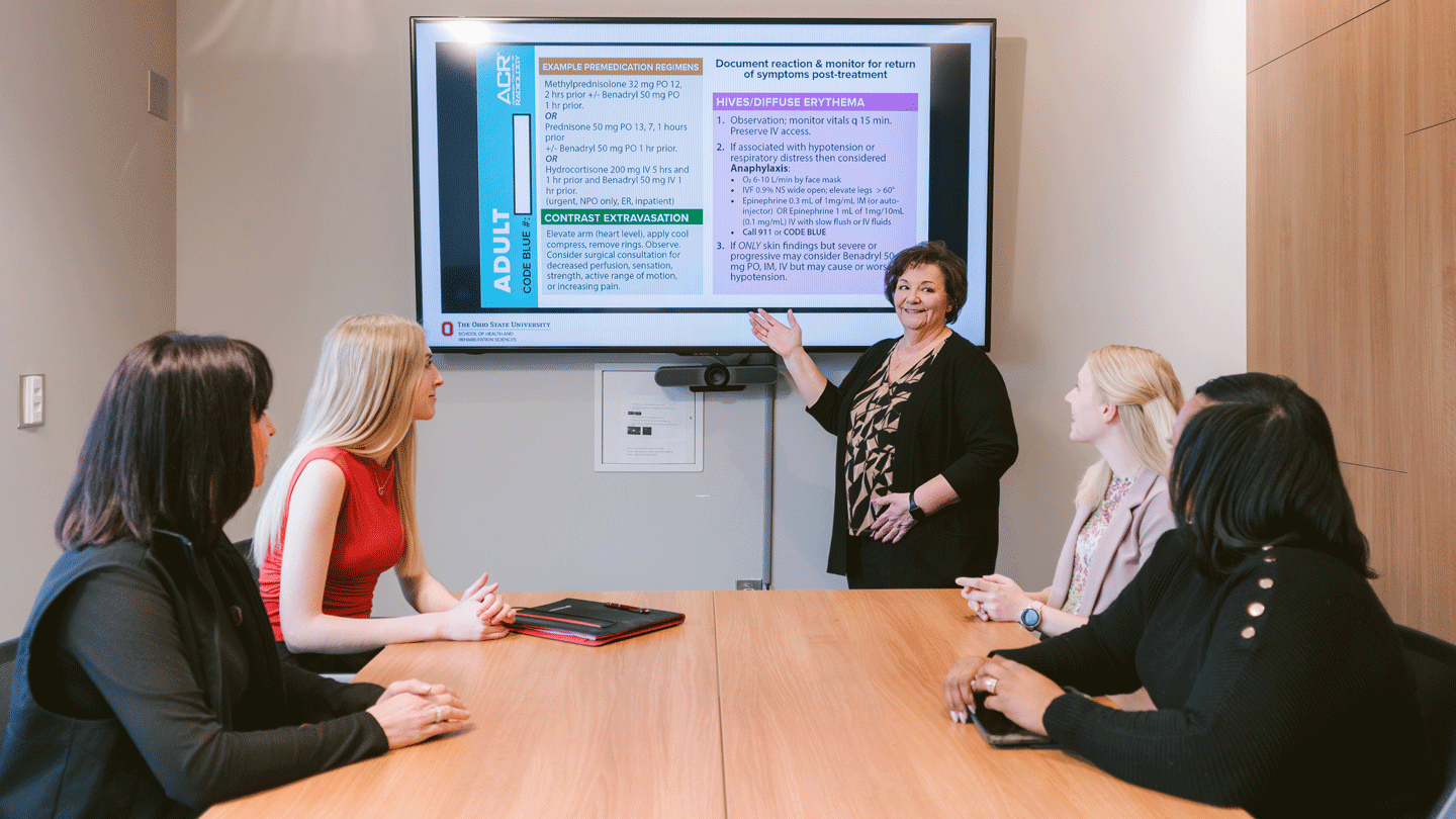 Tonette leading a team meeting presentation with four female imaging professionals sitting at a conference table listening.