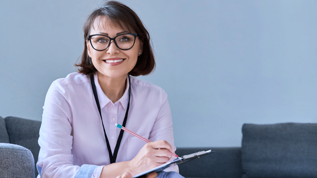 A professional woman with an clipboard sits on a couch.