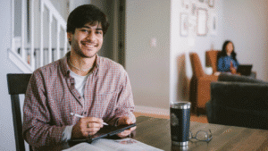 An online student sitting at a table with a tablet and textbook