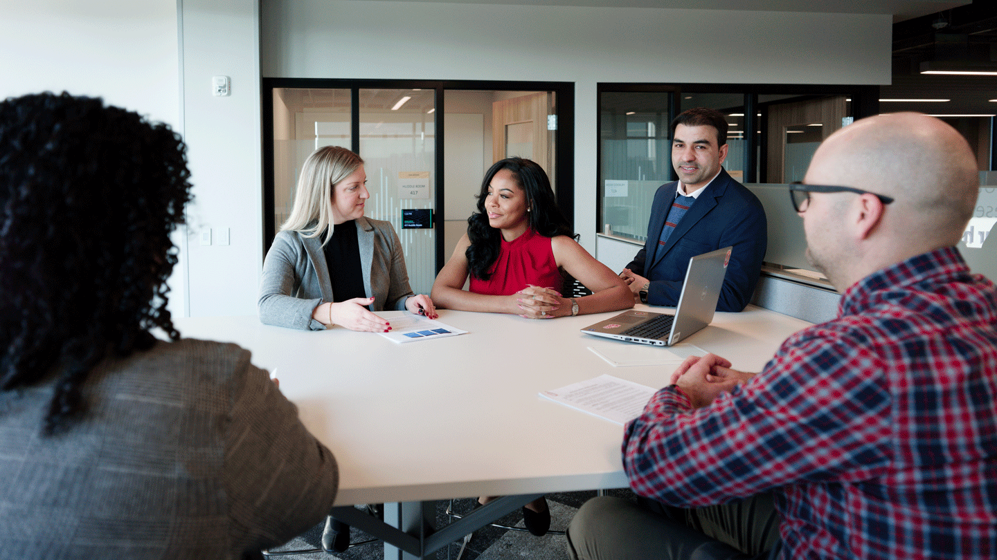 Group of five adult professionals sitting around a table collaborating.