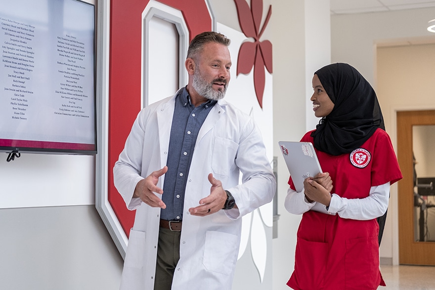 Nursing professional walking down hallway speaking to a woman